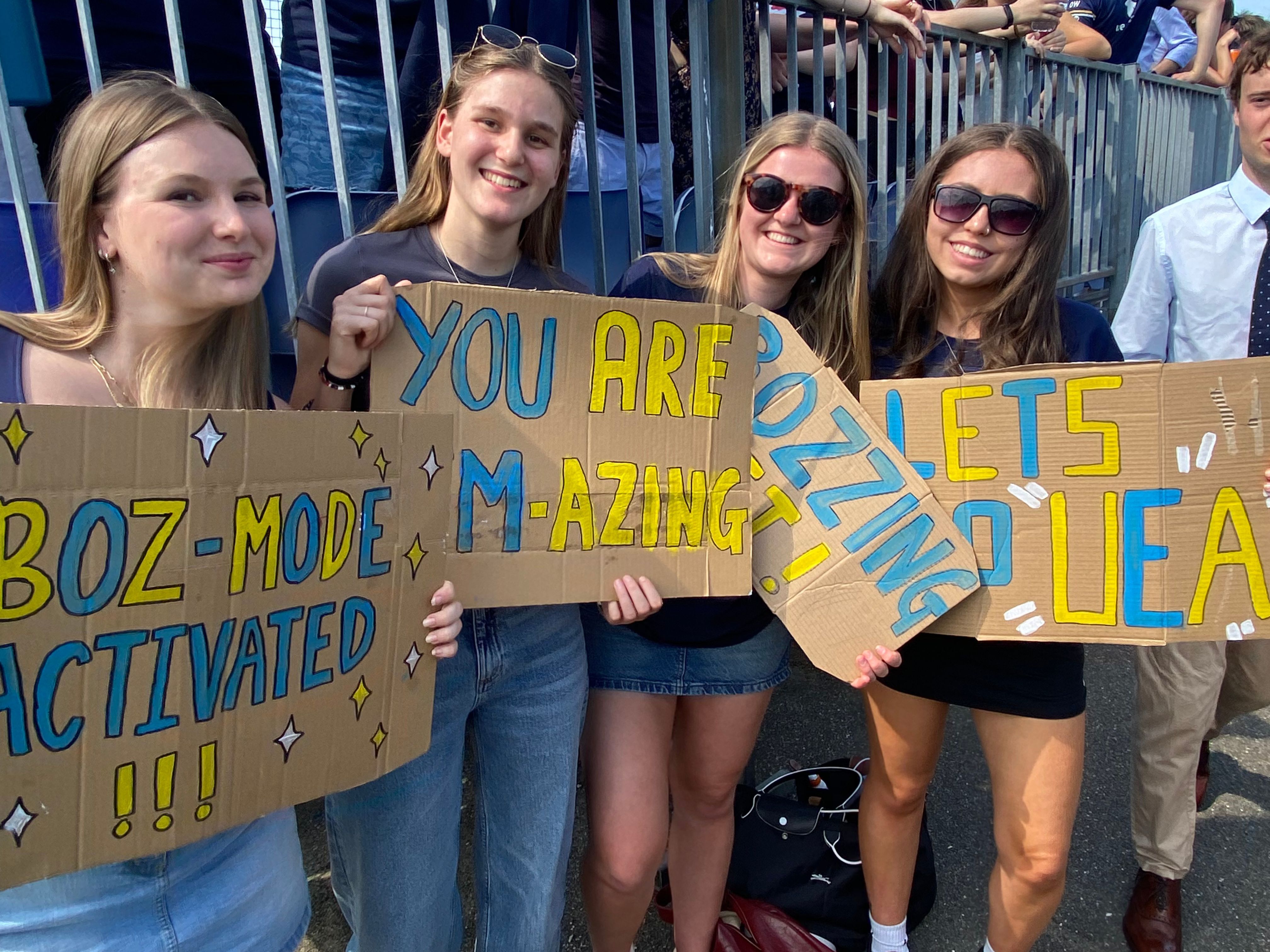 A photograph of students with handmade signs cheering on a sports team