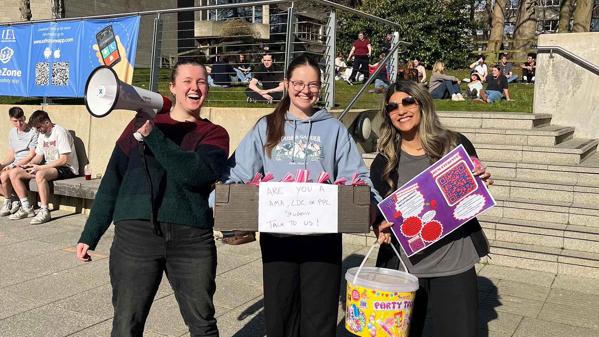 Three staff members laughing while collecting student feedback on campus in the sun